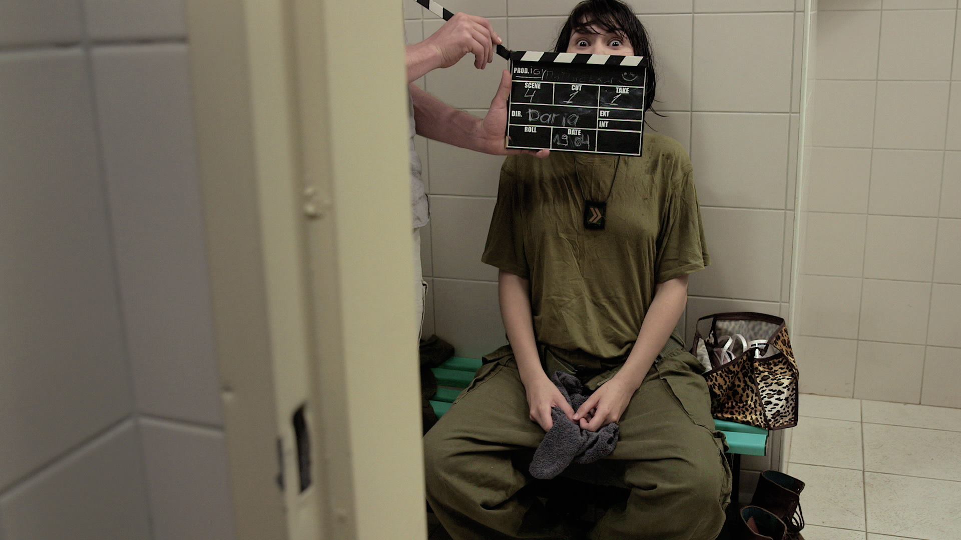 A person sits on a bench as an assistant director holds up a clapperboard on a film set.